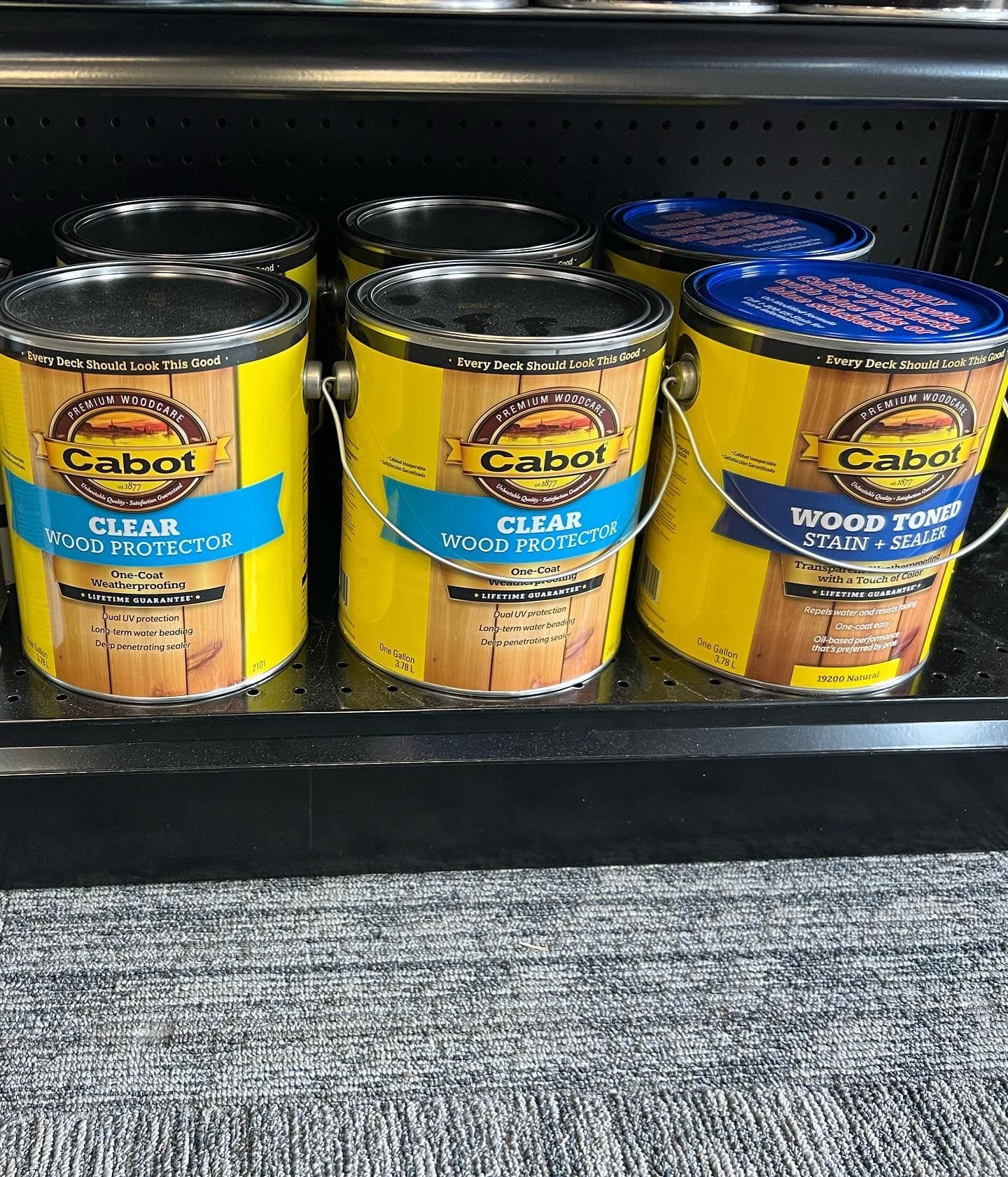 Three cans of cabot wood protector are sitting on a shelf.