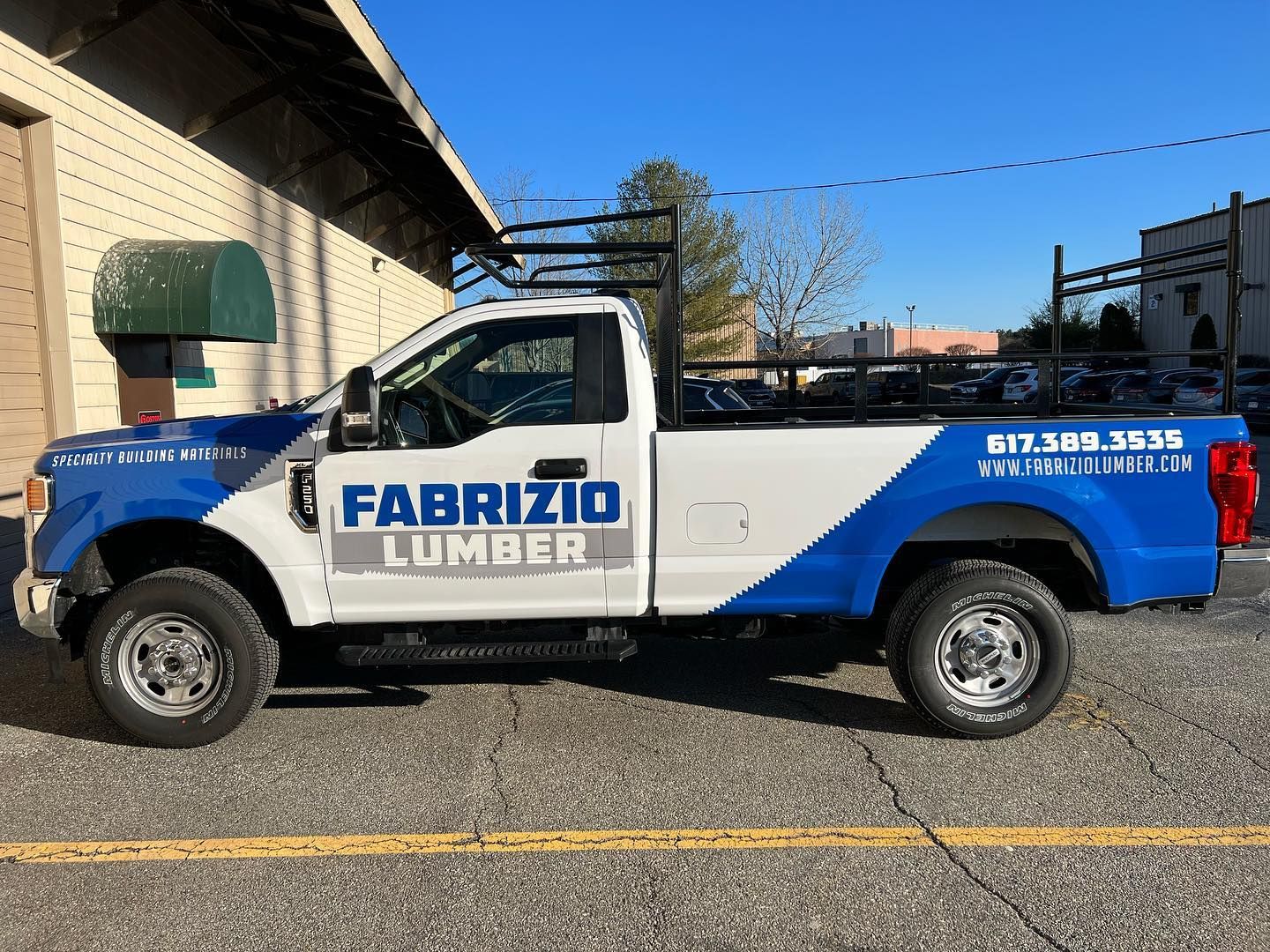 A blue and white lumber truck is parked in front of a building.