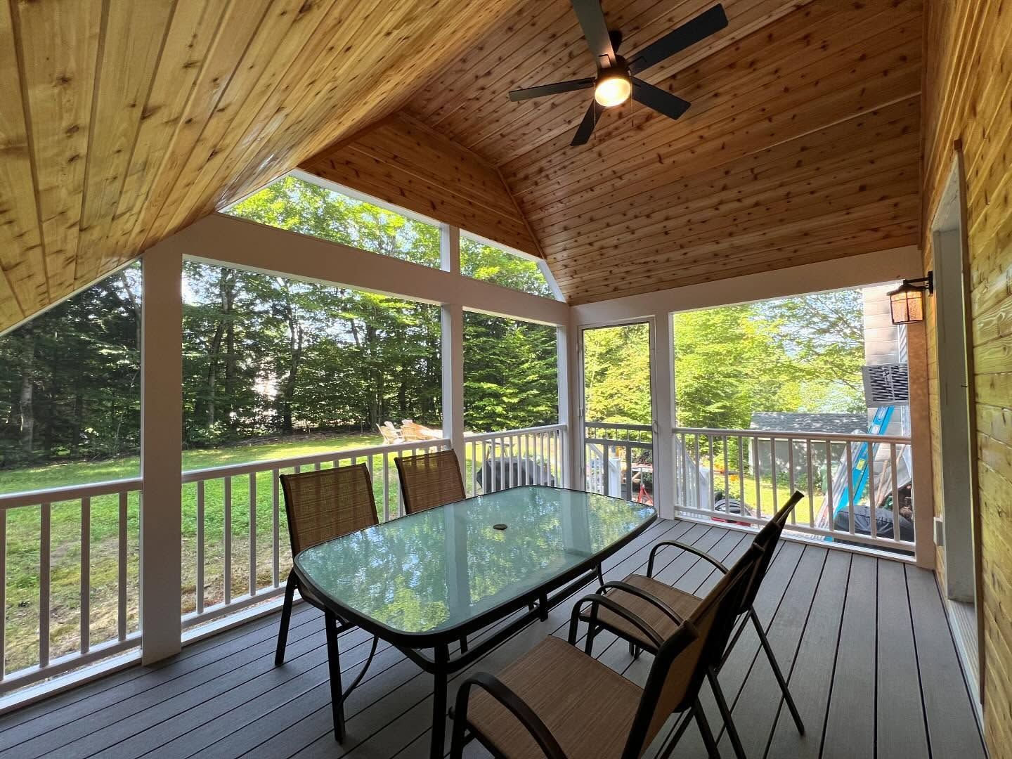 A screened in porch with a table and chairs and a ceiling fan.