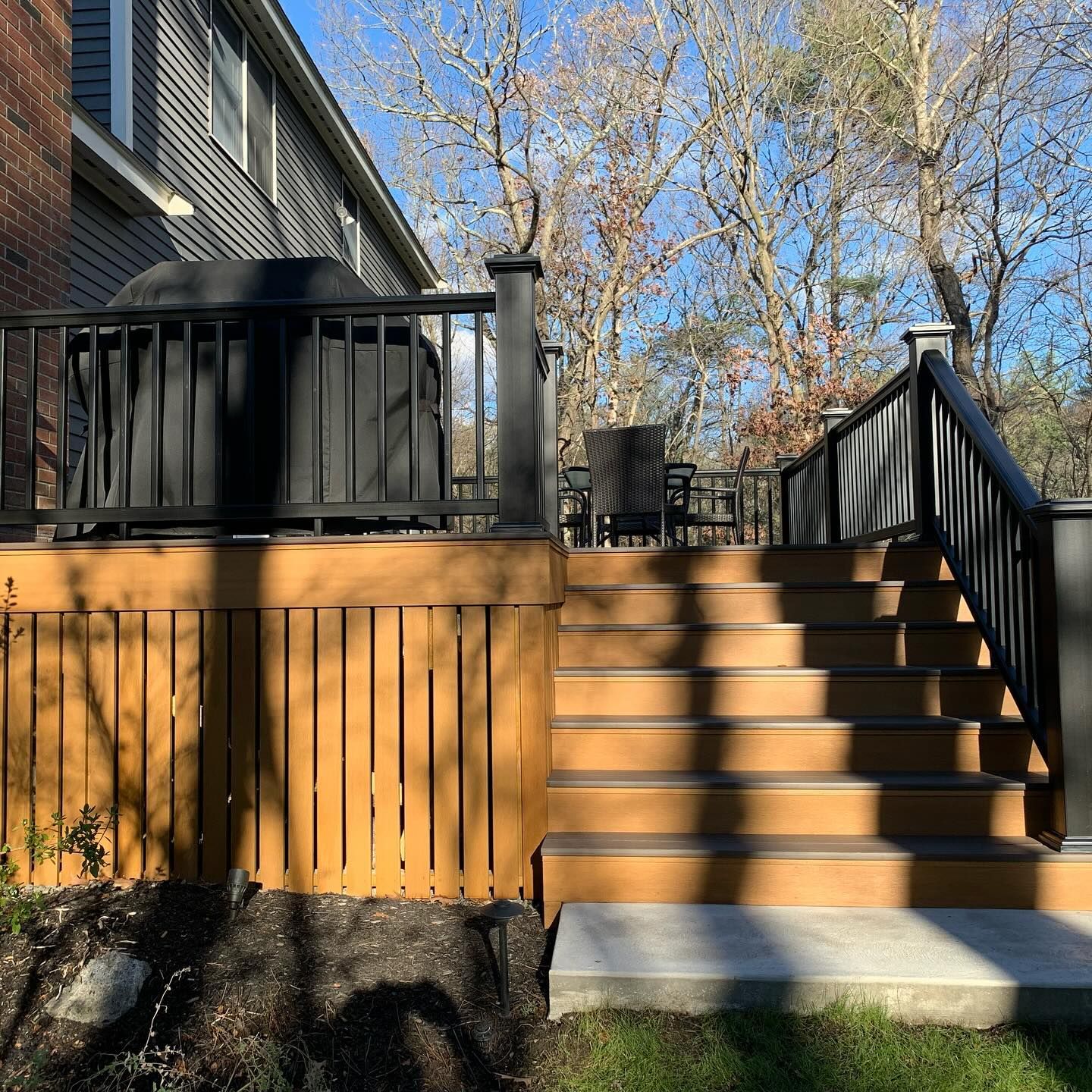 A wooden deck with stairs leading up to it and a black railing.