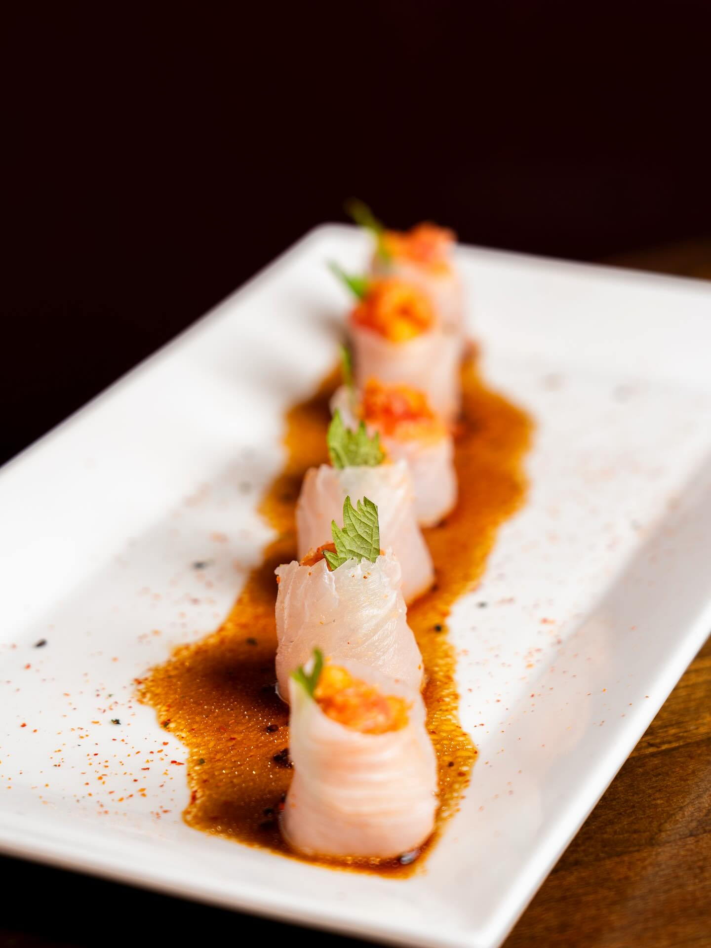 Sushi rolls on a white plate, drizzled with sauce and garnished with herbs.