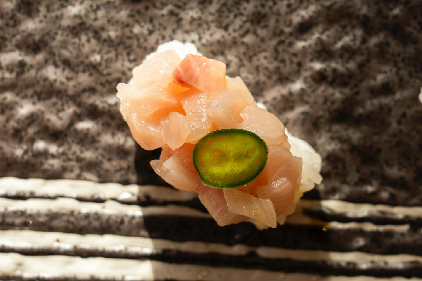 Sushi with chopped fish, green slice, on a patterned plate.