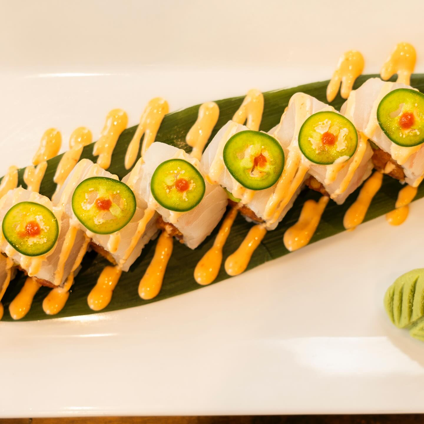 Sushi roll on a leaf, topped with jalapeño slices, orange sauce, and a dollop of caviar.