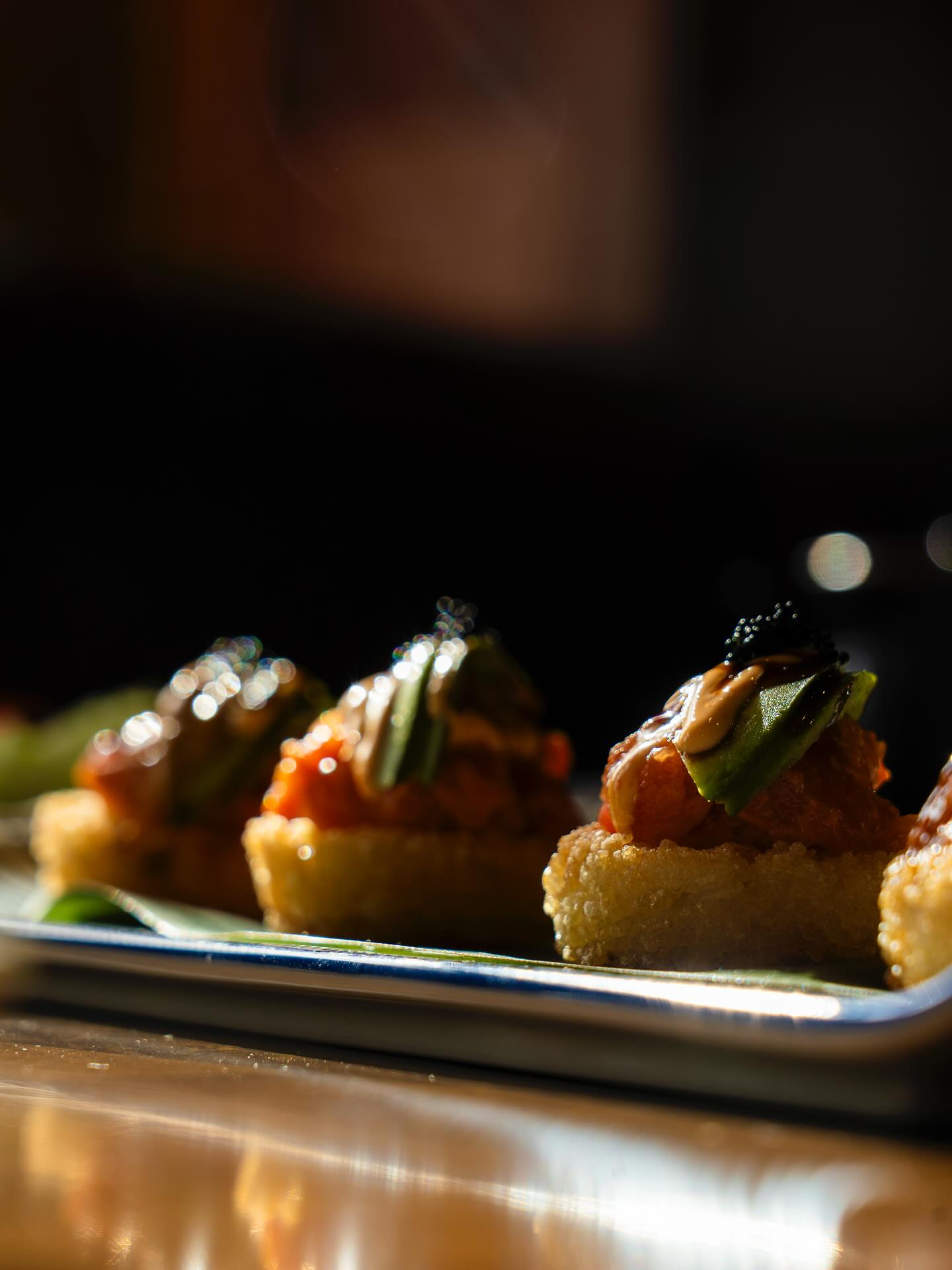 Sushi appetizers on a platter: crispy rice topped with spicy tuna, avocado, and black roe.
