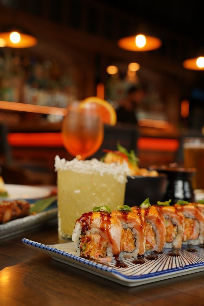 Sushi roll, margarita, and other dishes on a restaurant table, with bar lights in the background.