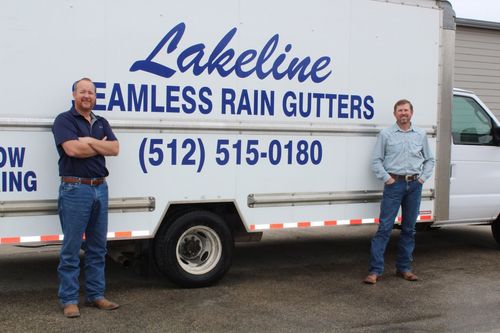 Two men standing by a white Lakeline Seamless Rain Gutters truck with phone number on the side