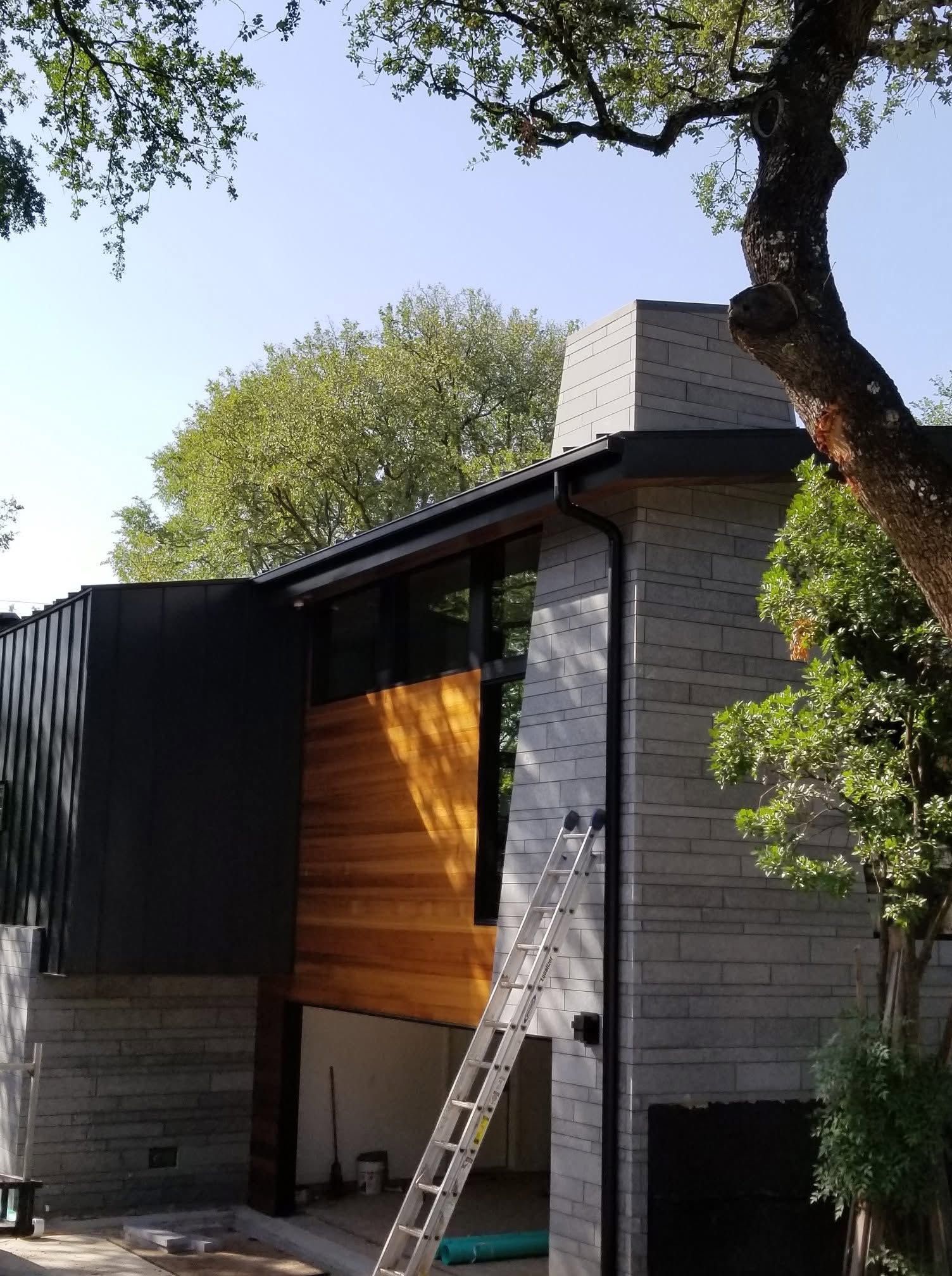 Two-story house exterior with a ladder against the wall and trees overhead
