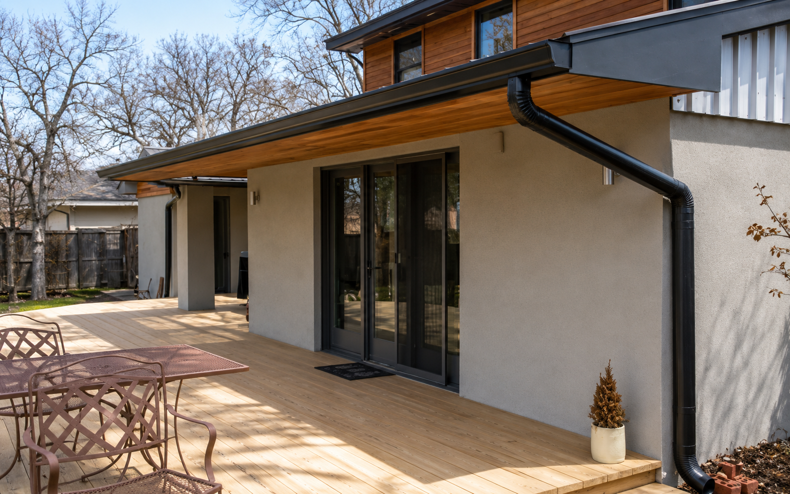 Patio with wicker tables and chairs beside a stucco house with sliding glass doors and wood eaves