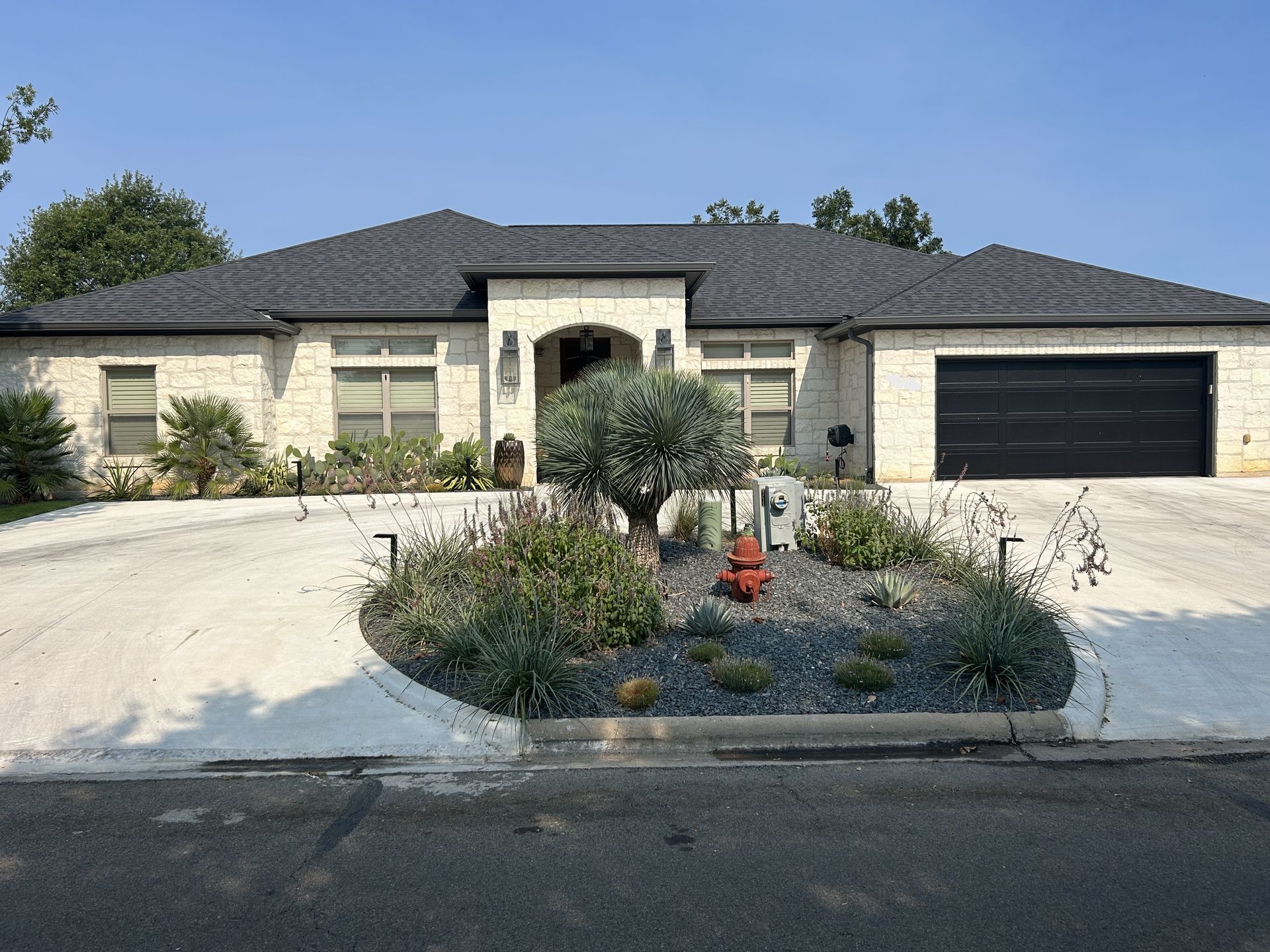 Single-story beige house with dark garage, white driveway, and desert landscaping in front.