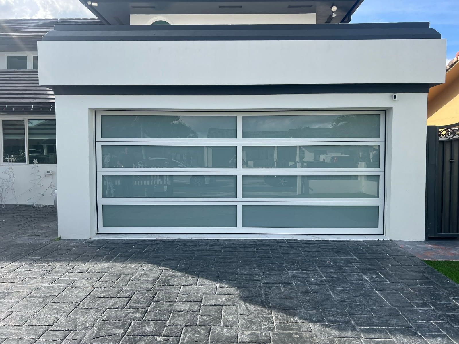 A white garage door with a lot of windows is sitting in front of a house.