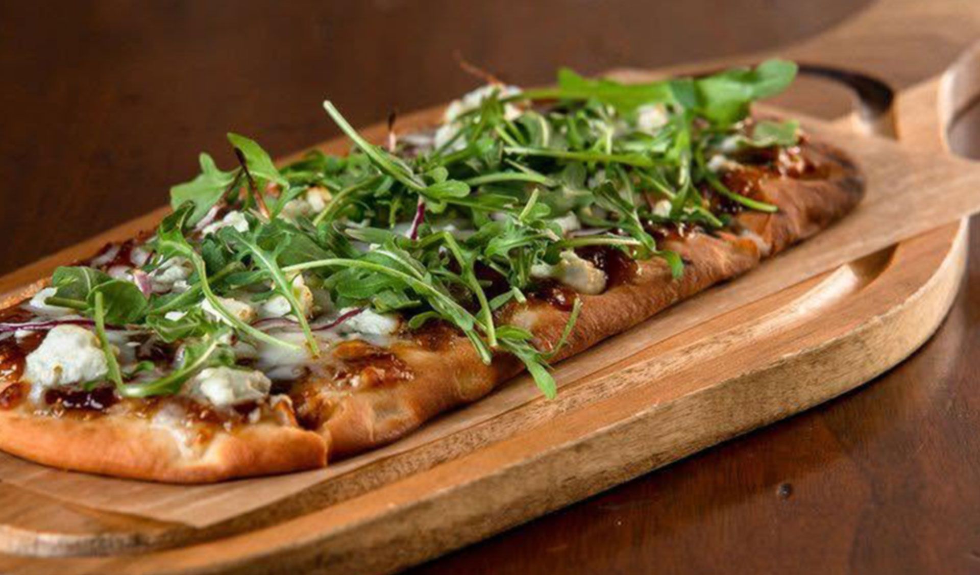 Flatbread topped with cheese and arugula on a wooden cutting board