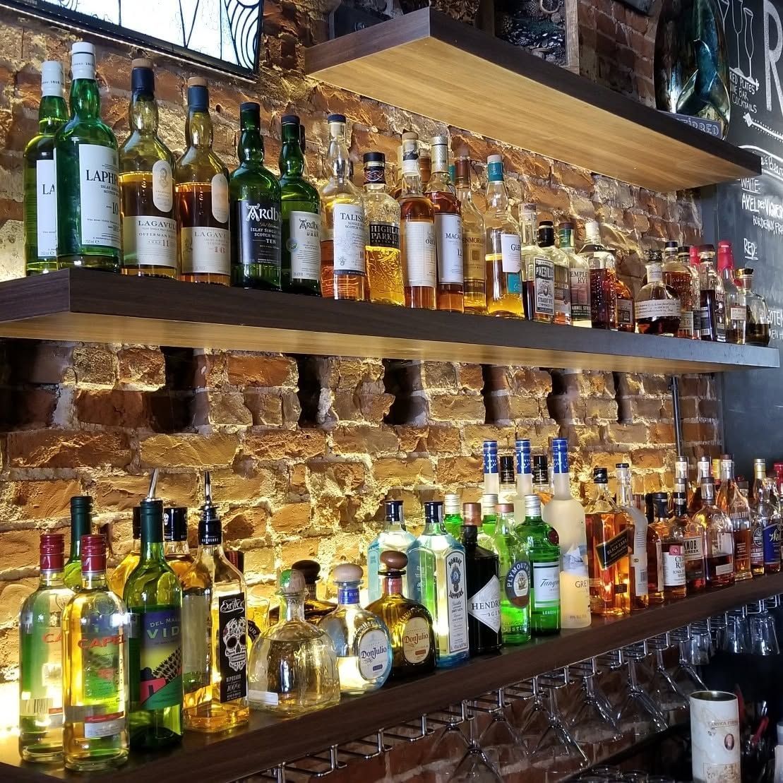 Shelves of assorted liquor bottles and glasses in a warmly lit bar against a brick wall