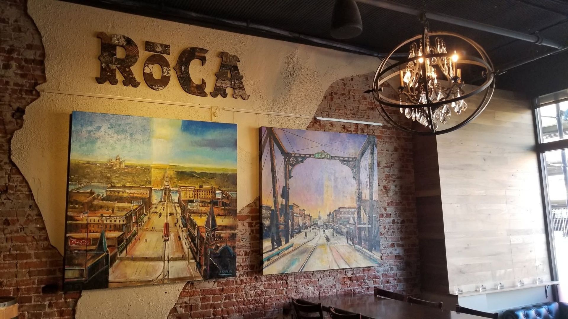Restaurant wall with “R&C” sign, two framed cityscape paintings, and a hanging industrial light fixture