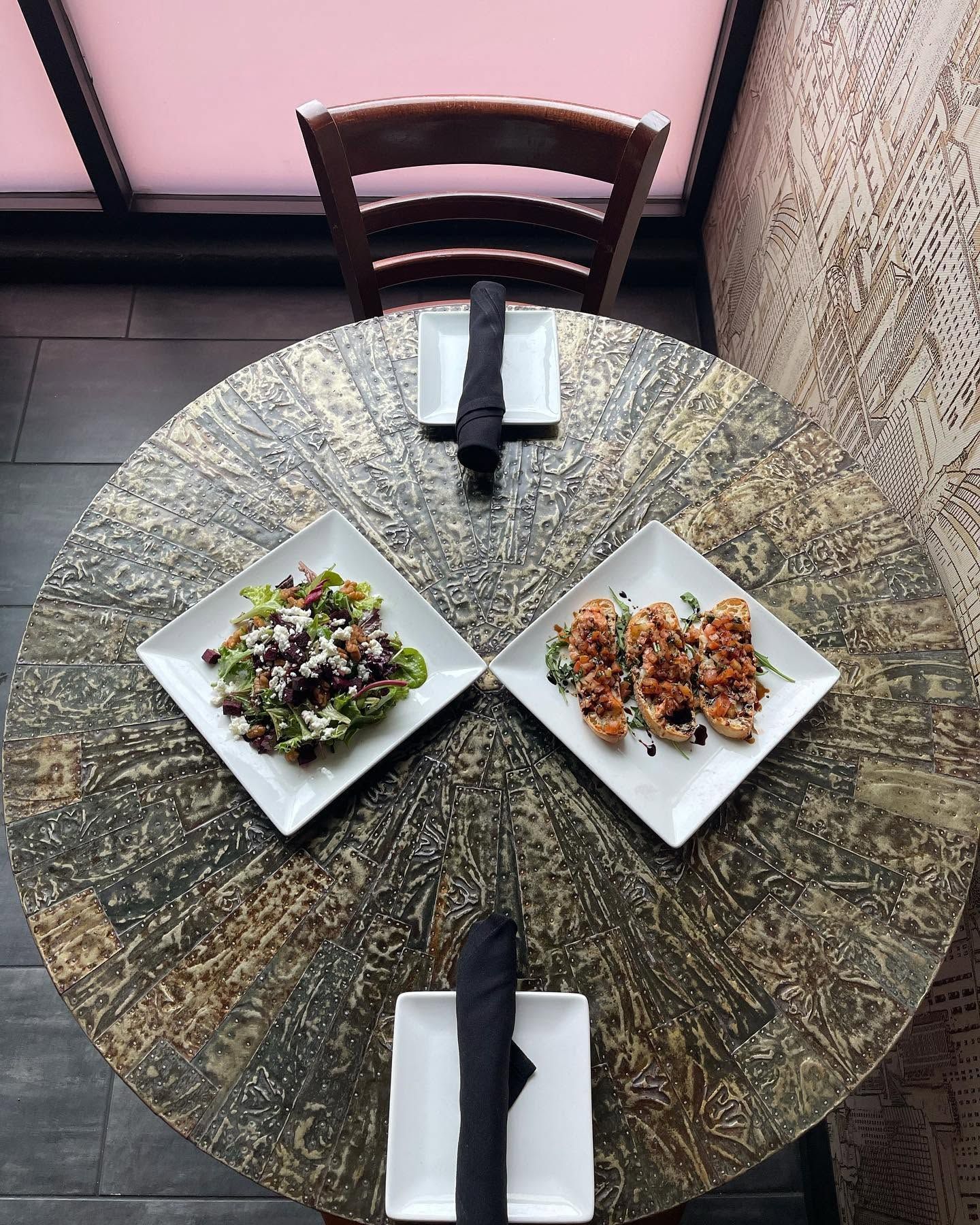 Two plated salads on a round table with black napkins, viewed from above in a café booth.