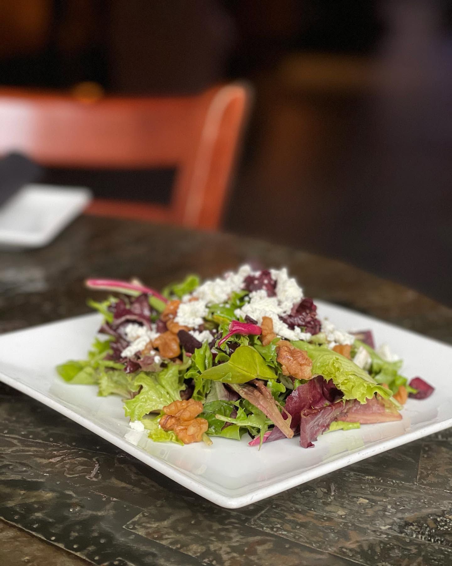 Colorful mixed salad with greens, feta, and berries on a white plate at a restaurant table