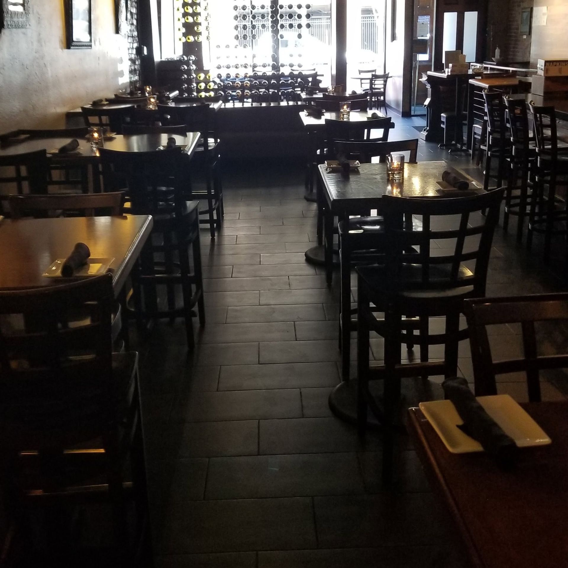 Empty restaurant dining room with dark wooden tables and chairs, dim lighting, and tiled floor