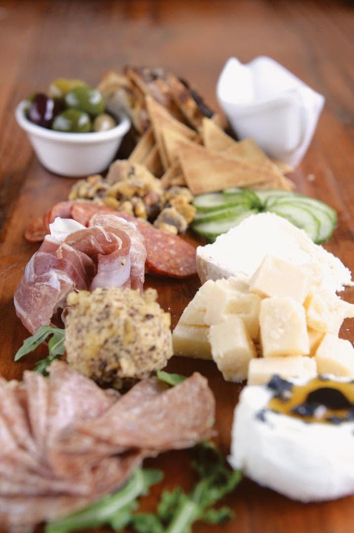 Assorted charcuterie board with cheese, cured meats, olives, crackers, and sliced avocado on a wooden table