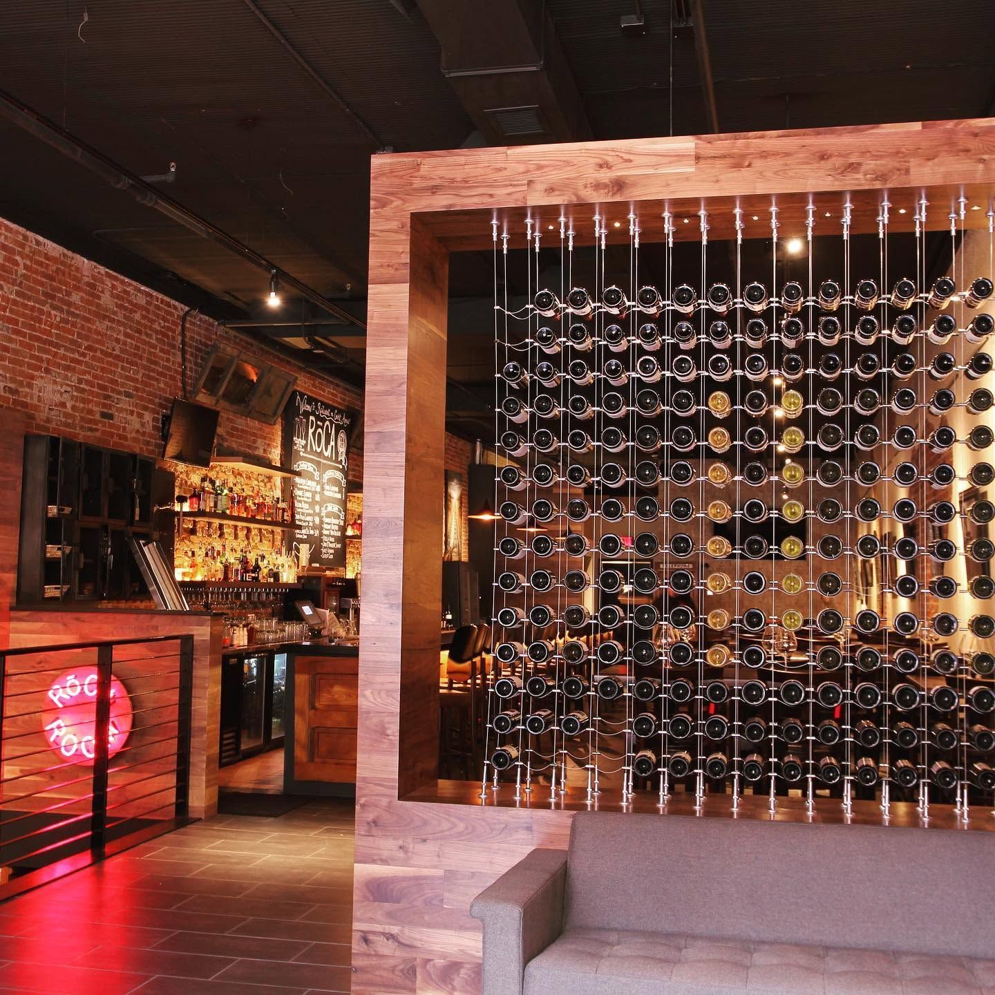 Modern bar interior with brick walls, a wine bottle display, and a hanging glass installation