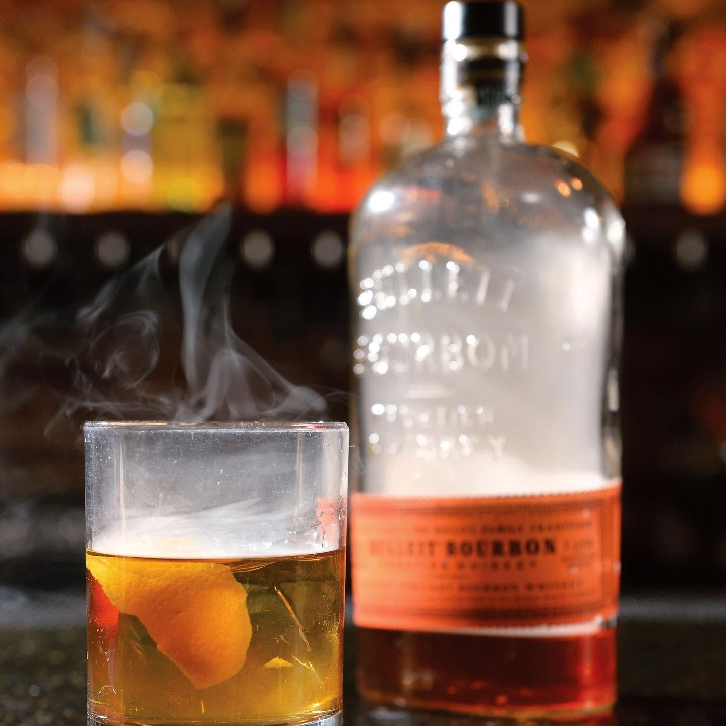 Whiskey cocktail in a rocks glass with citrus peel beside a whiskey bottle on a bar