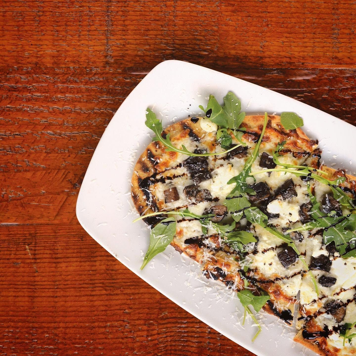 White plate with grilled flatbread topped with greens and drizzled dark sauce on a wooden table