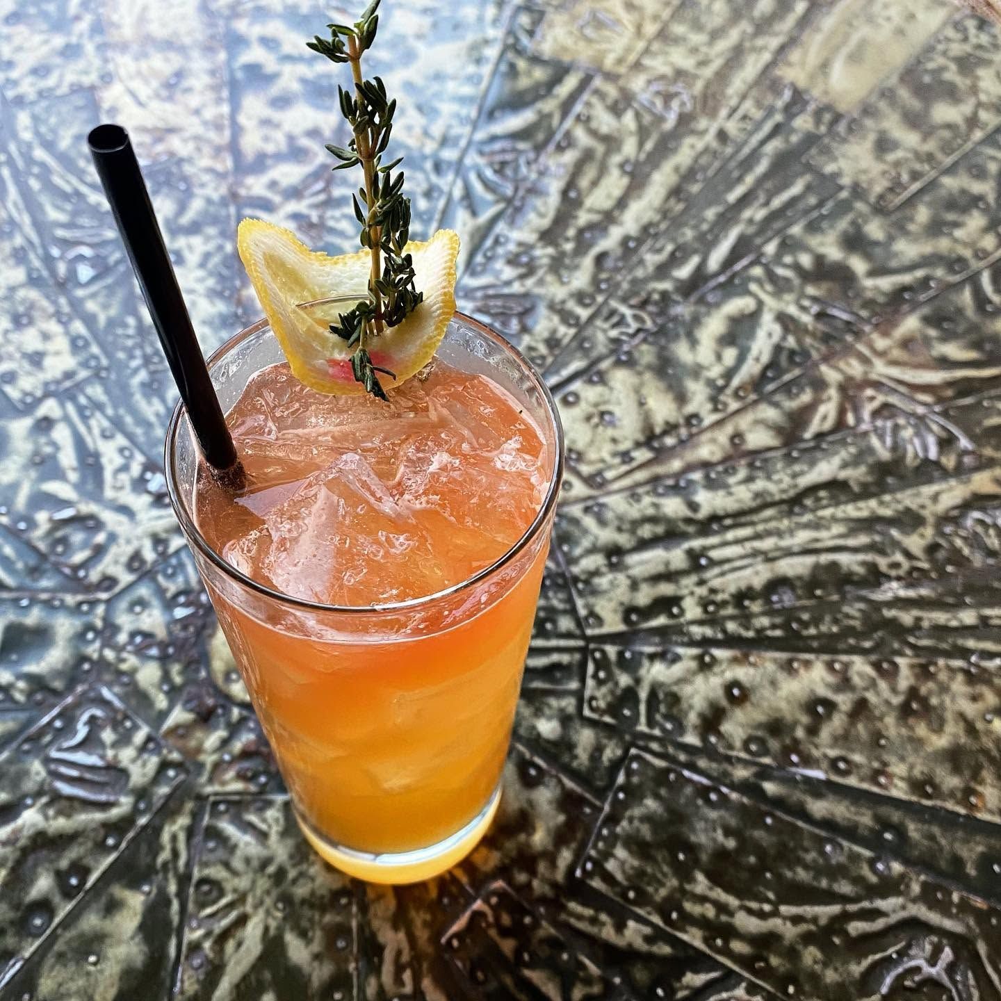 Orange cocktail with crushed ice, straw, and pineapple garnish on a patterned table