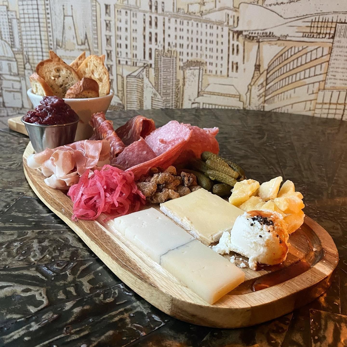 Charcuterie board with cheeses, meats, pickles, fruit, and bread on a table