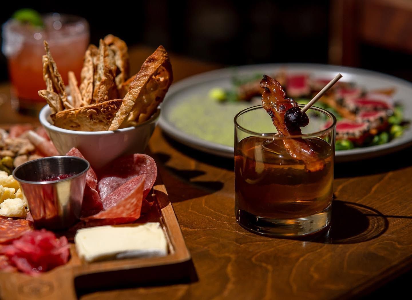 Assorted appetizers and cocktails on a wooden table in a dimly lit restaurant