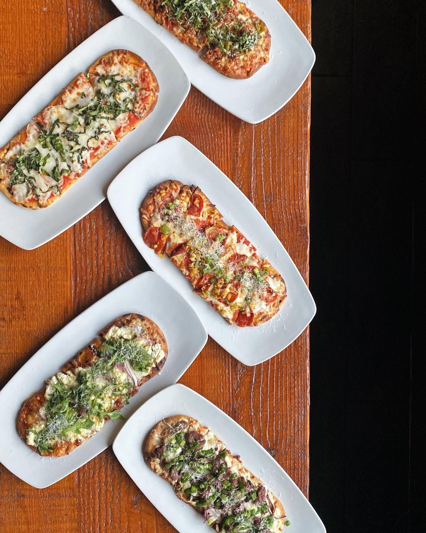 Five baked bread slices topped with herbs and sauce on white plates on a wooden table