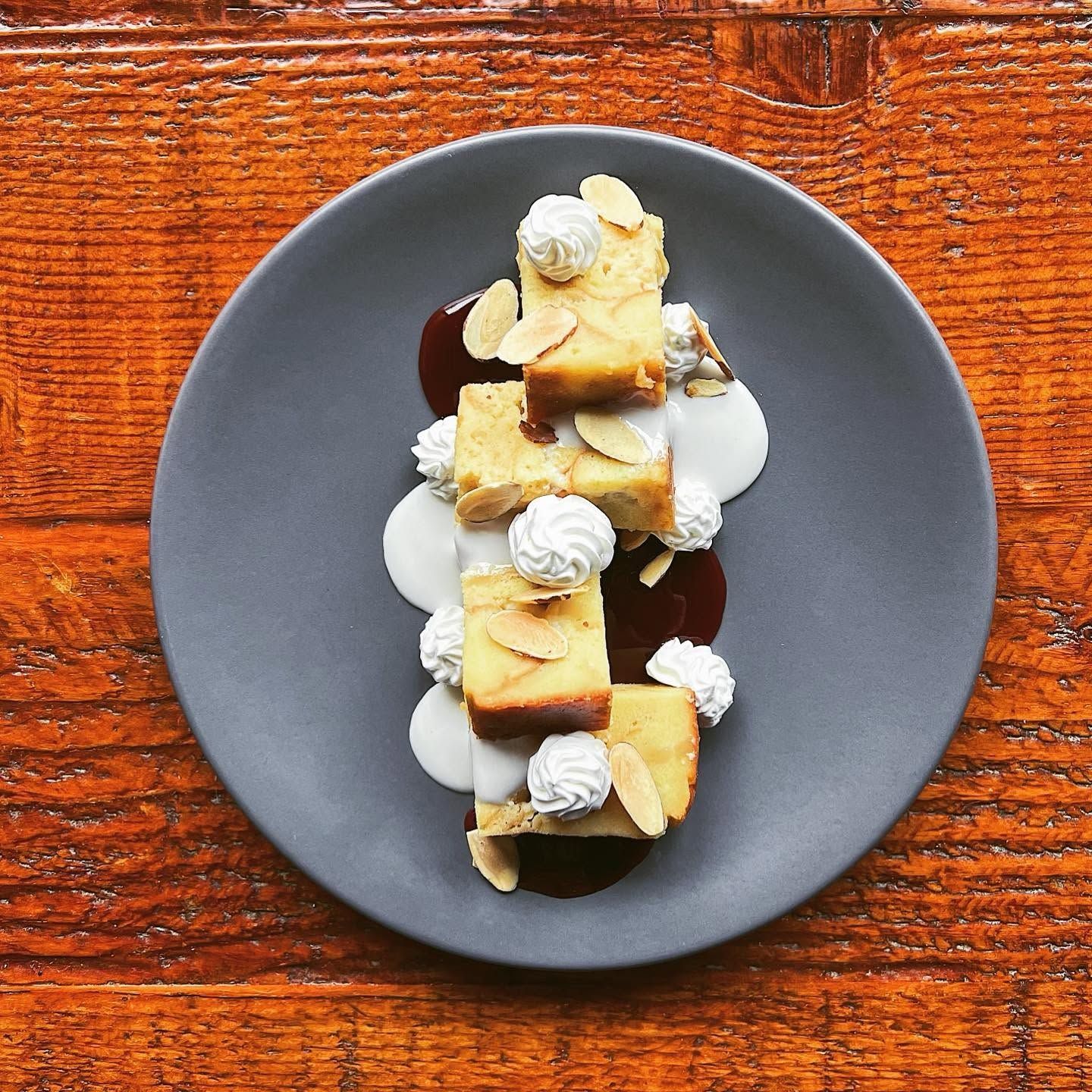 Dessert cubes drizzled with cream on a dark gray plate atop a wooden table