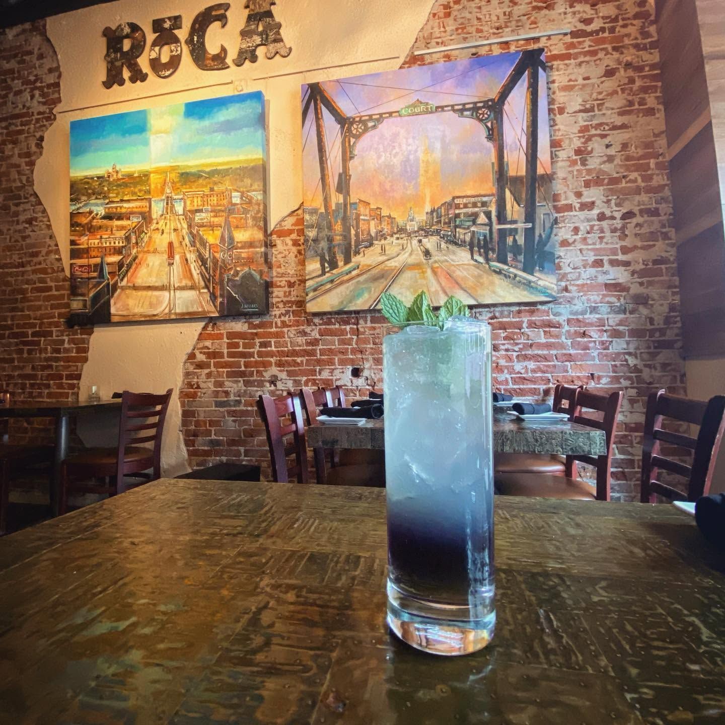 Rustic restaurant interior with brick wall art and a tall blue drink on a wooden table