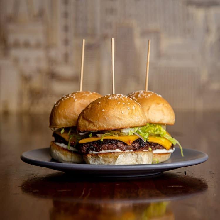 Three cheeseburgers with toothpicks on a dark plate against a blurred background