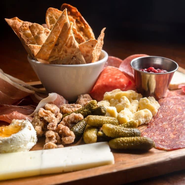 Assorted charcuterie board with crackers, cheeses, meats, pickles, nuts, and dipping sauce
