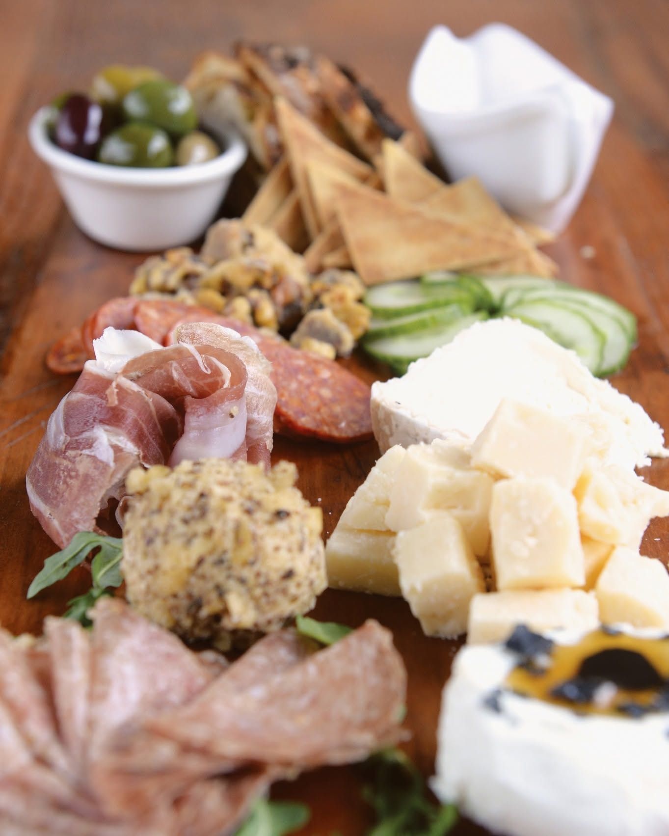 Charcuterie board with meats, cheeses, crackers, olives, nuts, and sliced cucumbers on a wooden table