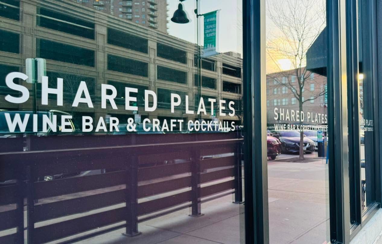 Shared Plates wine bar and craft cocktails sign on a storefront window at dusk