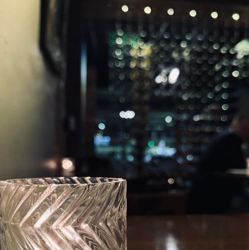 Glass candle holder on a table in a dimly lit restaurant with blurred city lights in the background