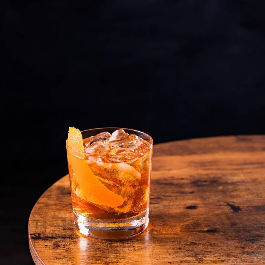 Orange cocktail with ice in a short glass on a wooden table against a dark background