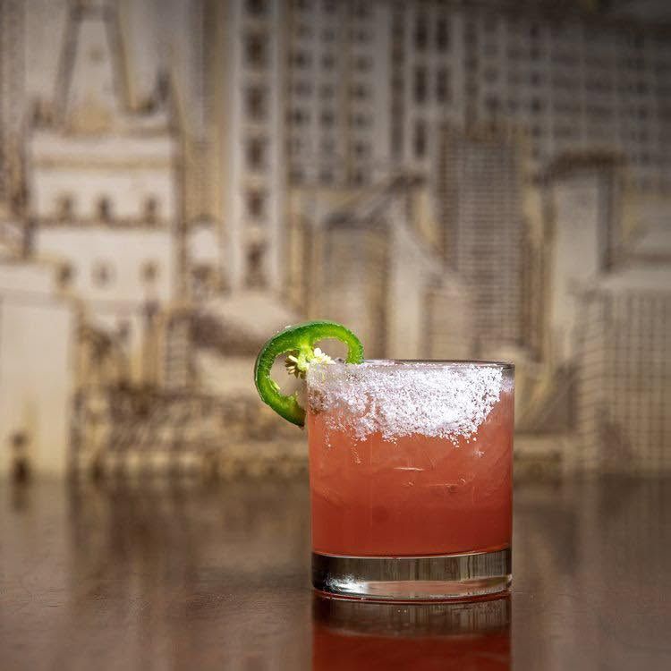 Pink cocktail in a short glass with a lime garnish and salted rim on a bar counter.