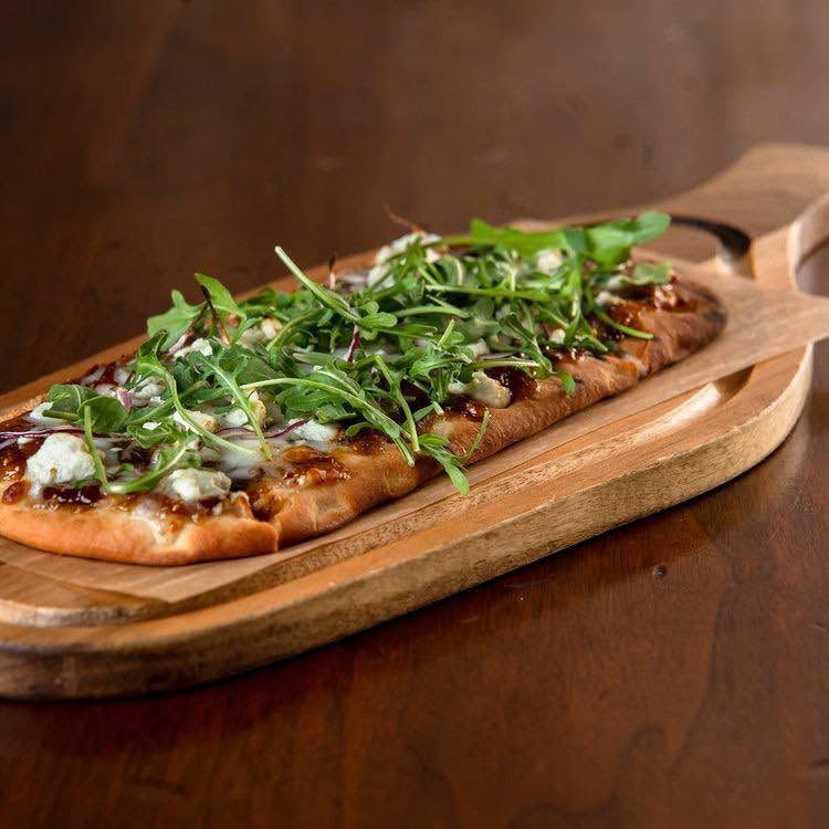 Flatbread pizza topped with greens and cheese on a wooden serving board