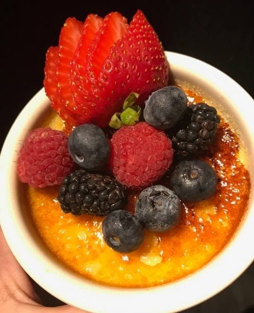 Bowl of crème brûlée topped with strawberries, blueberries, raspberries, and blackberries