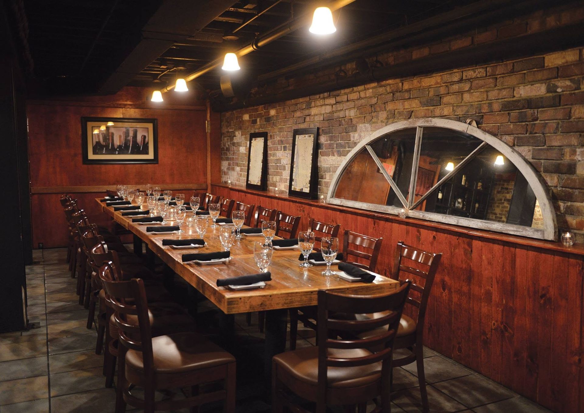 Empty rustic restaurant dining room with long wooden tables, brick walls, and warm hanging lights