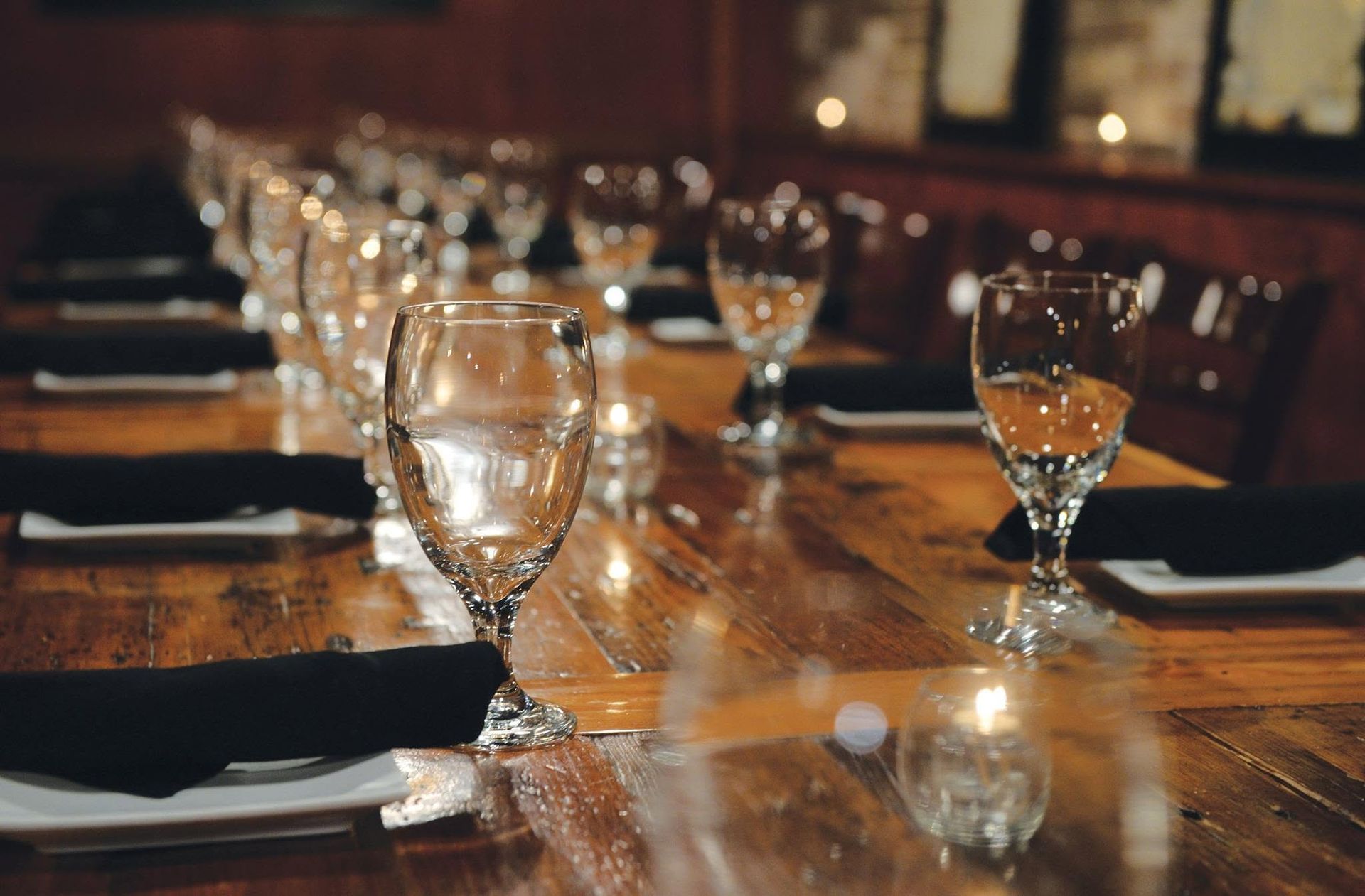 Set dining table with wine glasses, napkins, and candlelit reflections on a wooden table