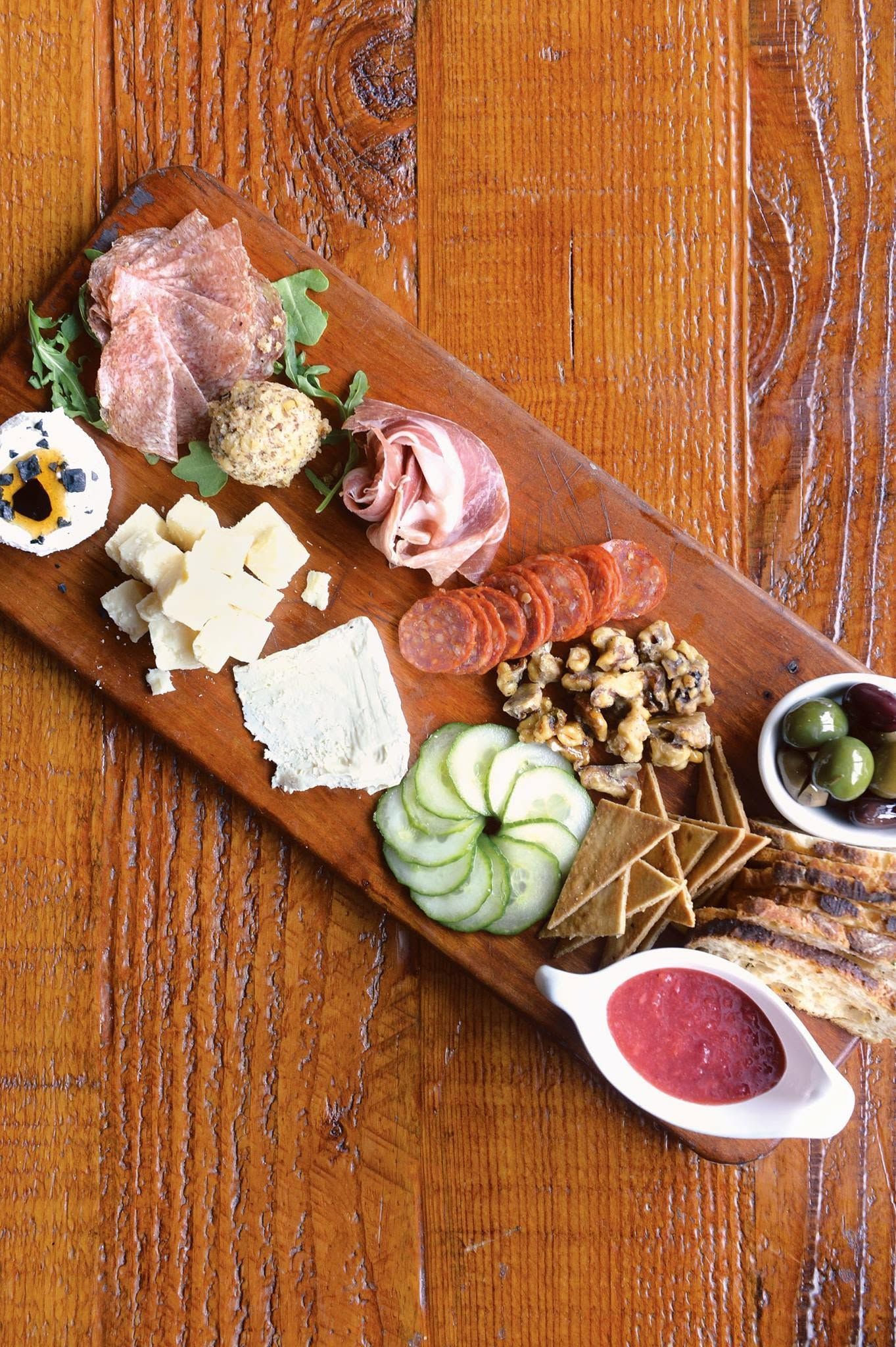 Assorted desserts and fruit arranged on a wooden board, with pink sauce in a small dish.