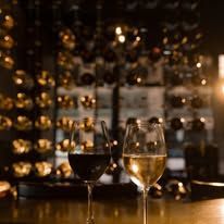 Two wine glasses on a bar, one red and one white, with warm bokeh lights and shelves in the background