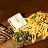 Grilled steak with fries, herbs, and dipping sauce on a wooden board