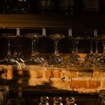 Wine glasses lined upside down on a bar shelf above bottles in warm, dim lighting