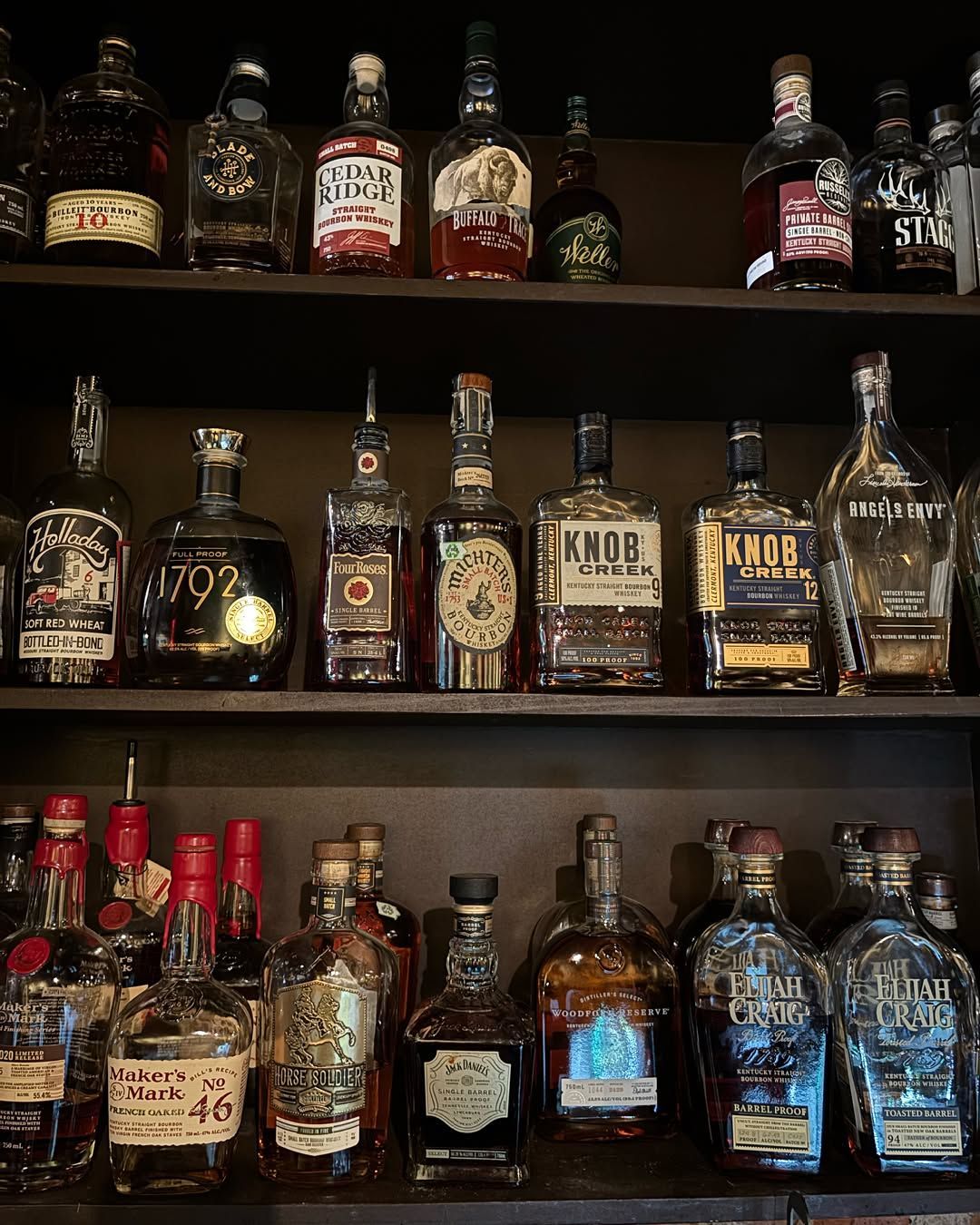 Shelves stocked with assorted whiskey and liquor bottles in a dim bar or store display