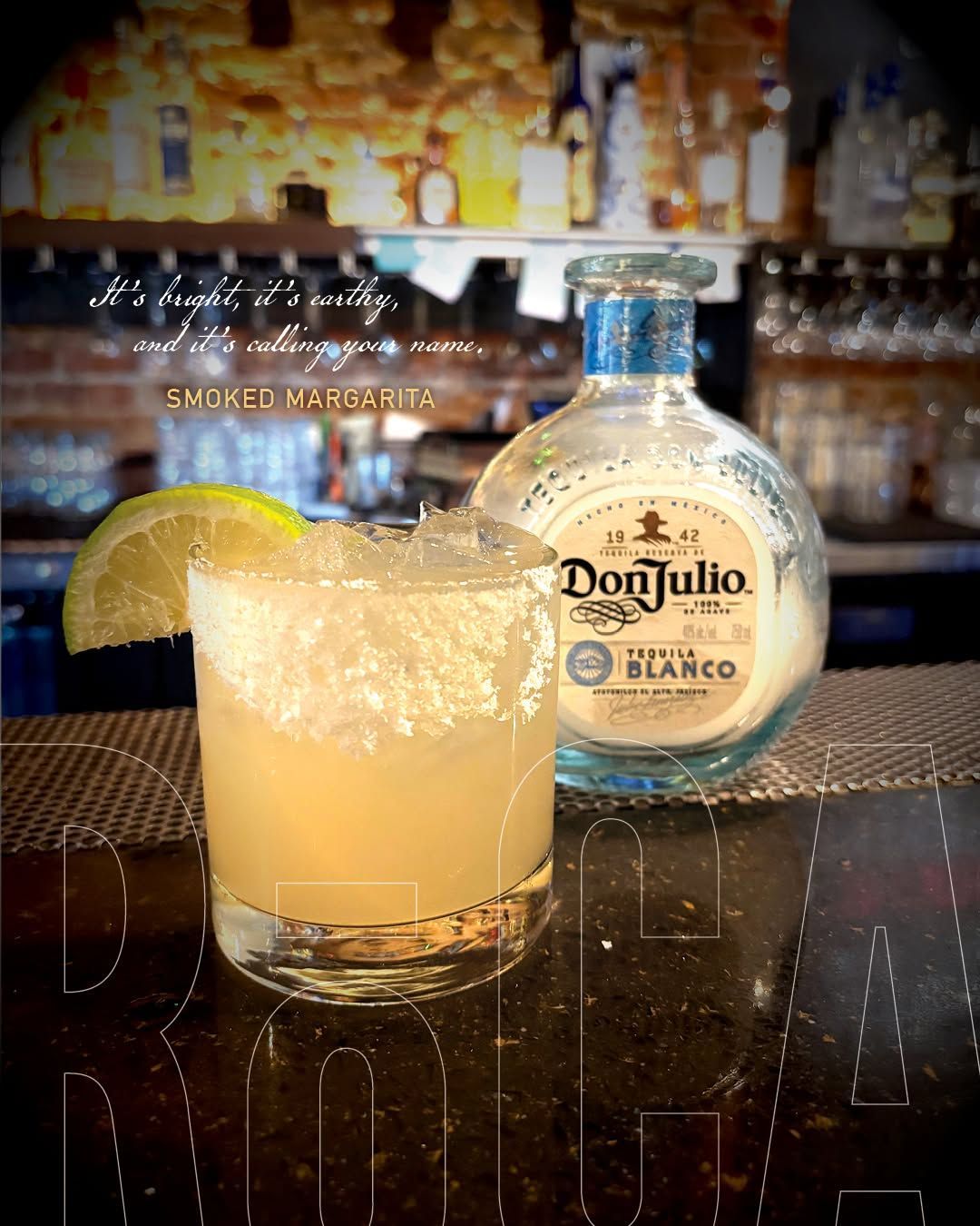 Tequila cocktail with lime wedge beside a Don Julio Blanco bottle on a bar counter