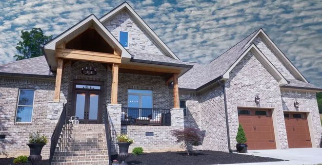 Large stone suburban house with a covered front porch and two-car garage under a partly cloudy sky