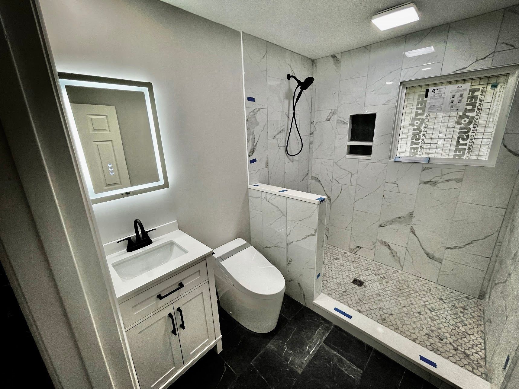 Modern bathroom with white vanity, toilet, and glass shower with marble tile.