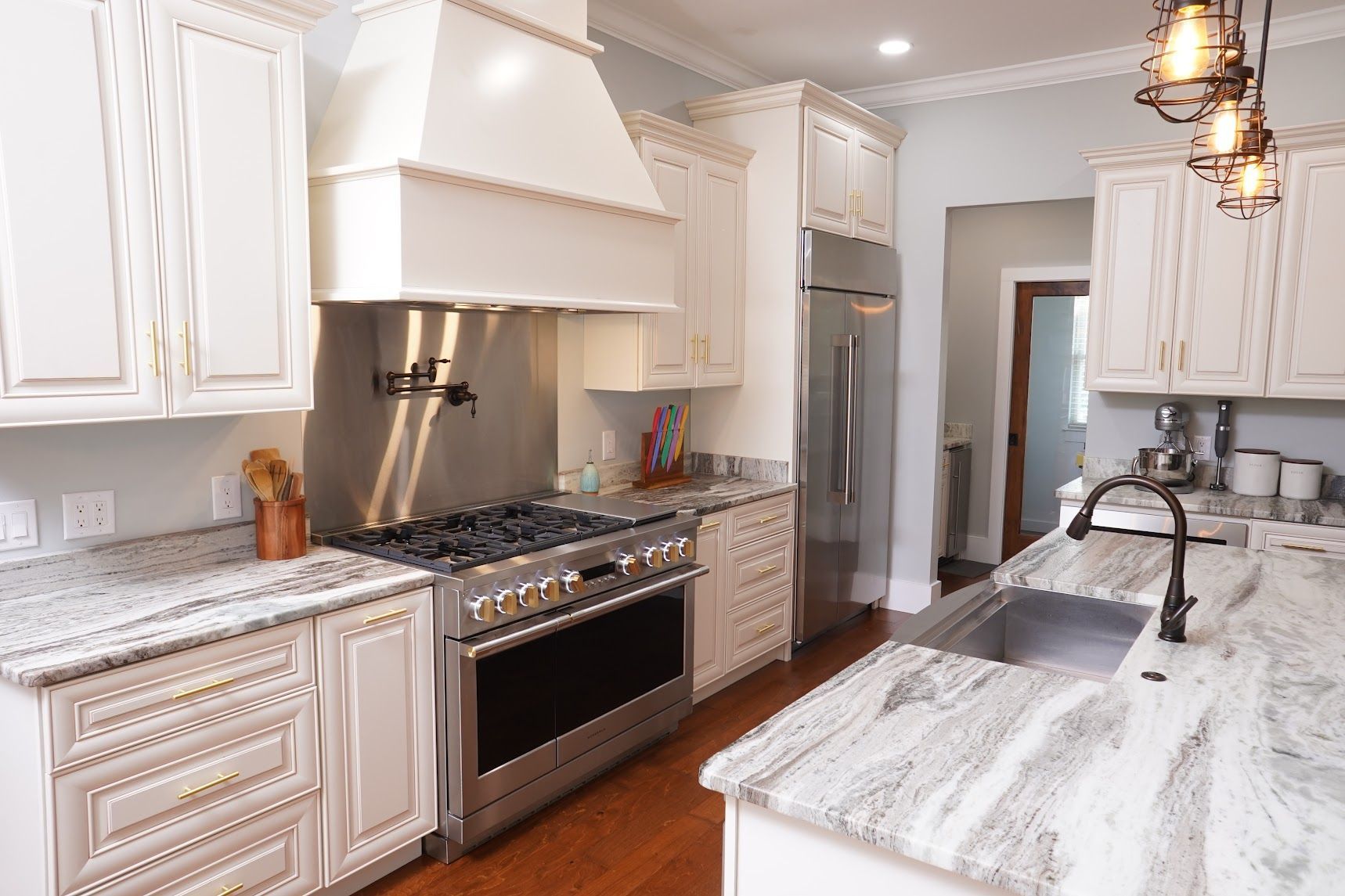 Bright white kitchen with marble island, stainless steel stove, and pendant lights